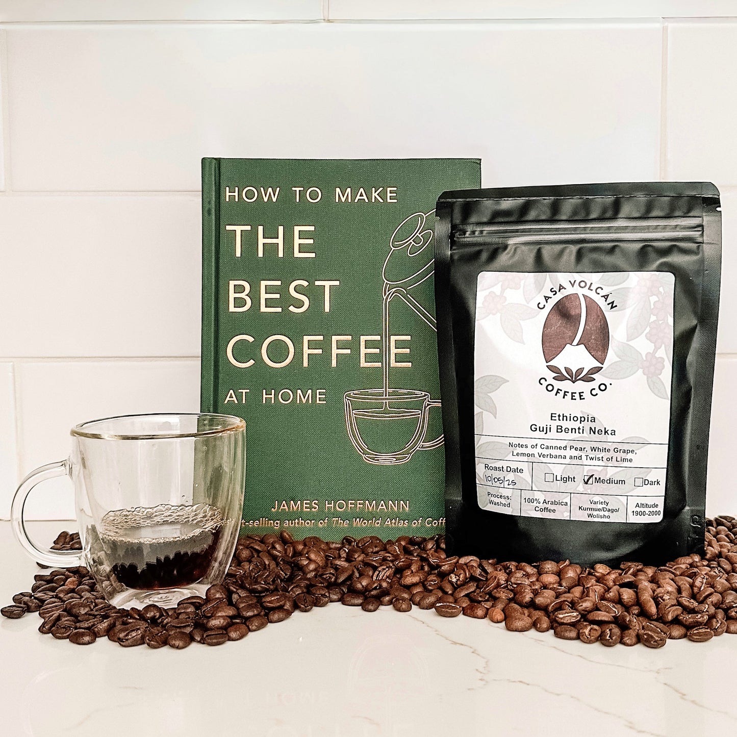 Coffee beans, a glass of coffee, a book on making coffee, and a coffee package on a white surface.
