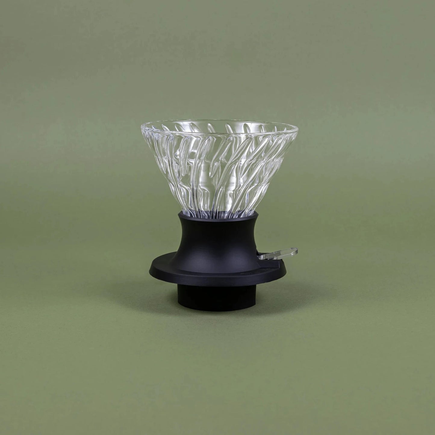Clear glass coffee dripper on a black base against a green background